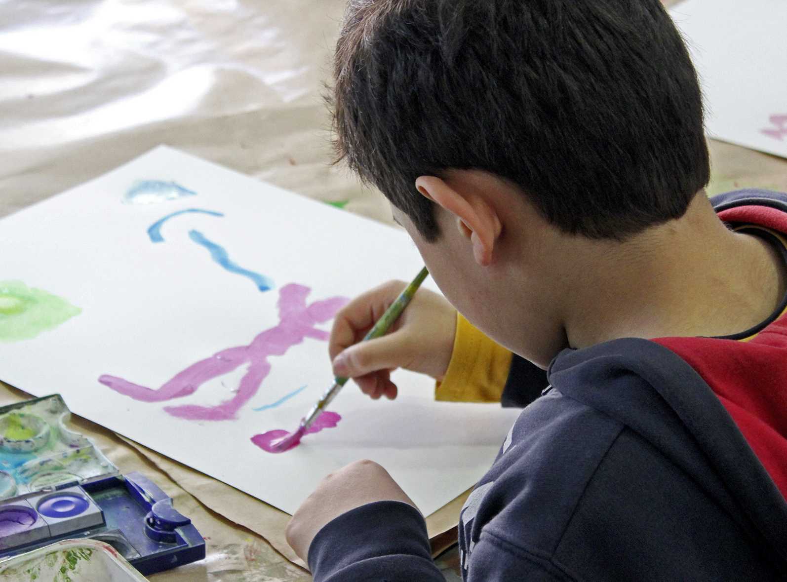 Die Abbildung zeigt einen Jungen von hintern, der gerade mit Wasserfarben auf einem Blatt Papier malt. Die Fotoaufnahme stammt von Thomas Ruppenstein.