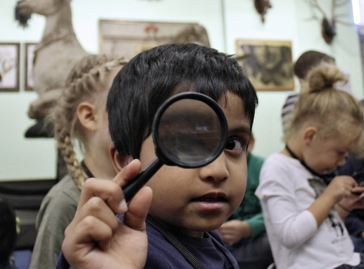 Die Abbildung zeigt eine Gruppe von Kindern im Germanischen Nationalmuseum. Ein Junge im Vordergrund blickt durch eine Lupe in die Kamera. Die Fotoaufnahme stammt von Thomas Ruppenstein.