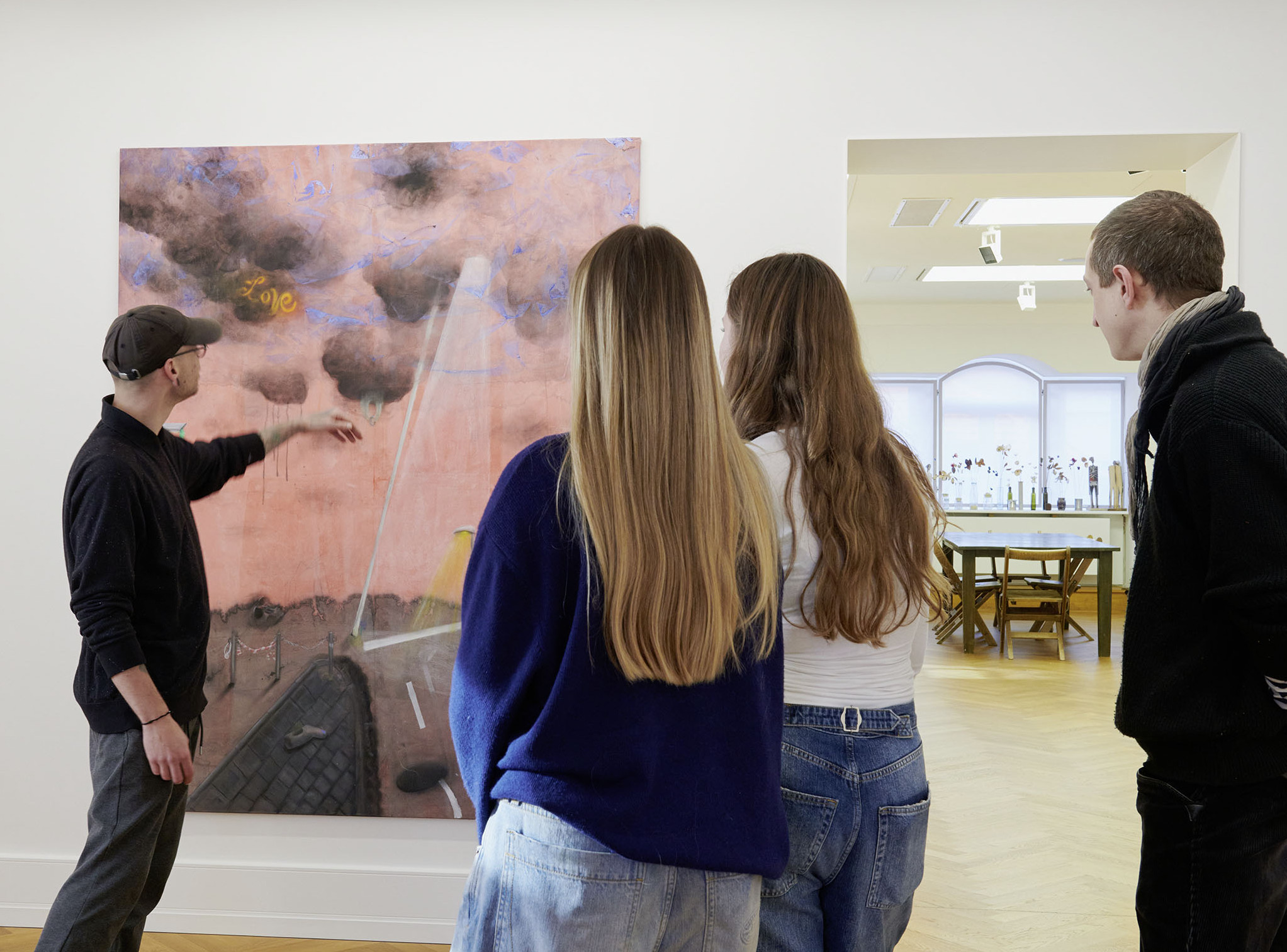 Die Fotoaufnahme zeigt drei Personen, zwei Frauen und ein Mann, vor einem Gemälde in der Ausstellung "Borgo Ensemble". Ein anderer Mann deutet auf ein Detail des Gemäldes und scheint es den anderen zu erläutern. Die Fotoaufnahme stammtm von Annette Kradisch.