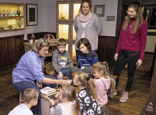 Die Fotoaufnahme zeigt Kinder und ihre Eltern bei ihrer Entdeckungstour im Albrecht-Dürer-Haus. Ein Mädchen riecht dabei gerade an einem kleinen Fläschchen mit einer Duftprobe. Die Fotoaufnahme stammt von Oliver Frank.