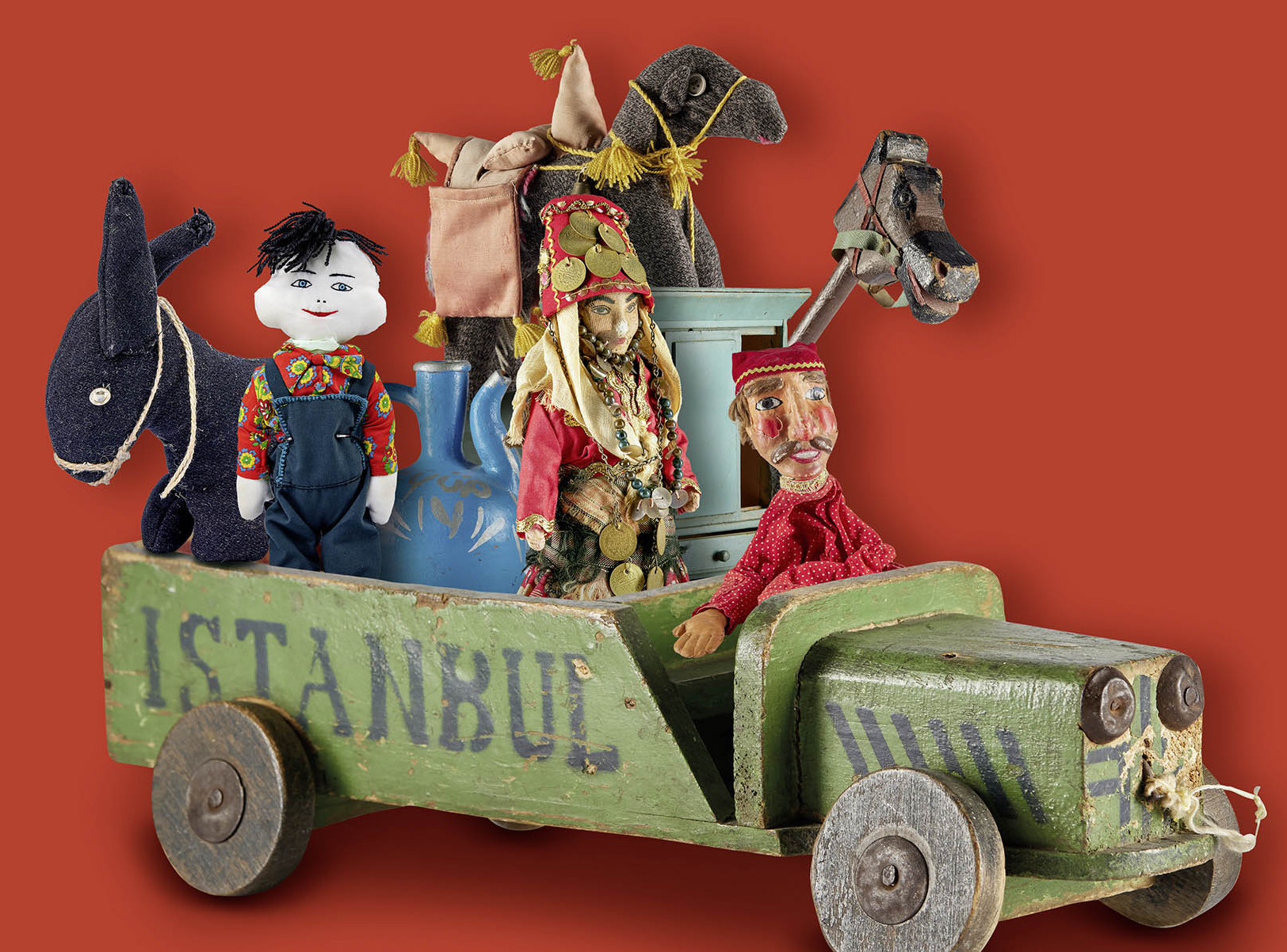 Die Abbildung zeigt eine Objektcollage, bestehend aus verschiedenen Spielzeugfiguren, die in einem Holzspielzeuglastwagen sitzen, auf dem Istanbul steht. Die Fotoaufnahme stammt vom Spielzeugmuseum. 