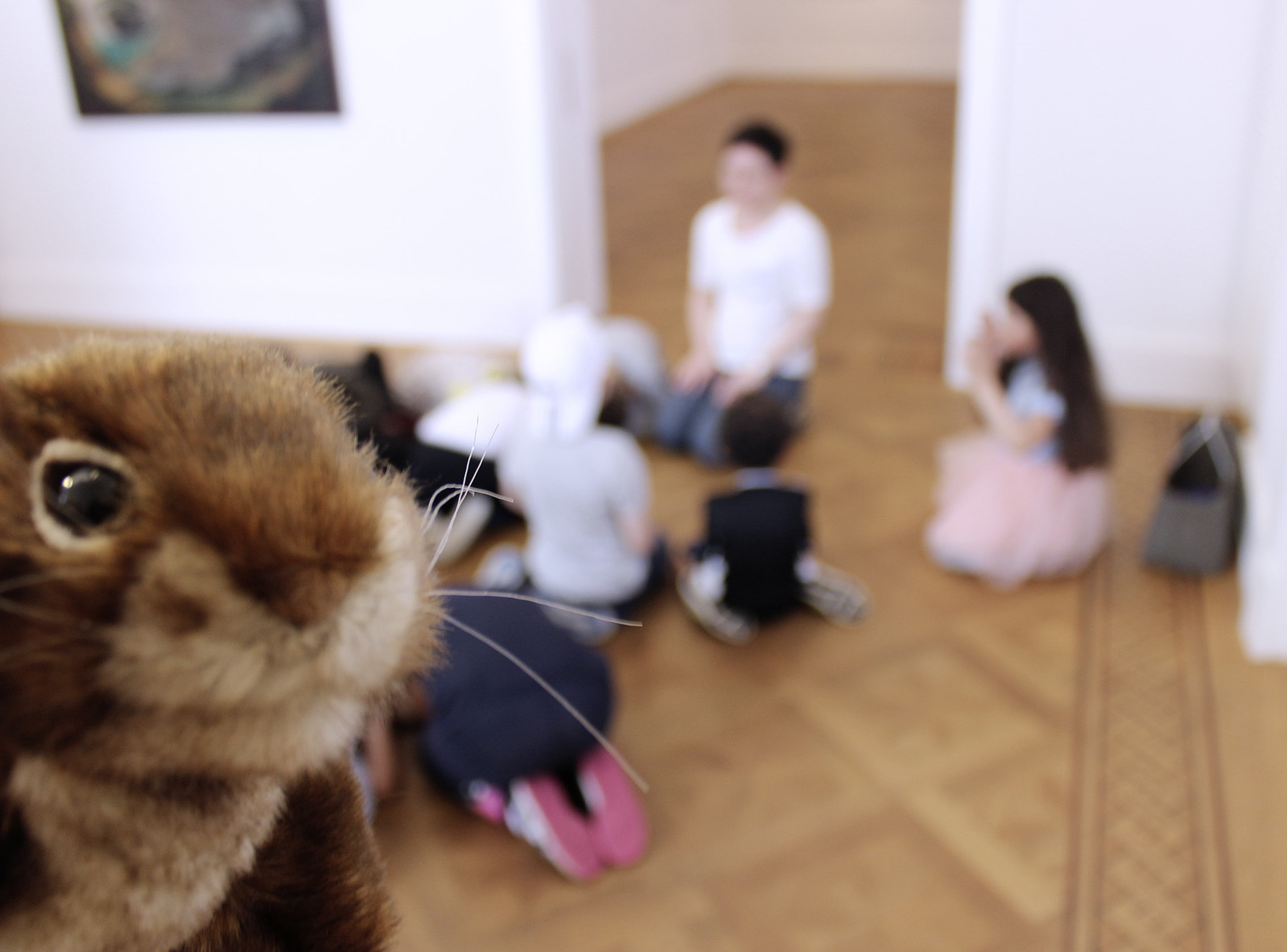 Die Abbildung zeigt im Hintergrund eine Kindergartengruppe in der Kunstvilla. Die Plüsch-Handpuppe Elli Eichhörnchen schaut im Vordergrund von links in die Kamera hinein. Die Fotoaufnahme stammt von Thomas Ruppenstein.