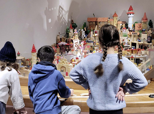 Die Abbildung zeigt drei Kinder im Grundschulalter, die im Spielzeugmuseum das Stadtmodell aus Spielzeug betrachten. Die Kinder stehen mit dem Rücken zur Kamera und schauen auf das Modell. Die Aufnahme stammt von Thomas Ruppenstein.