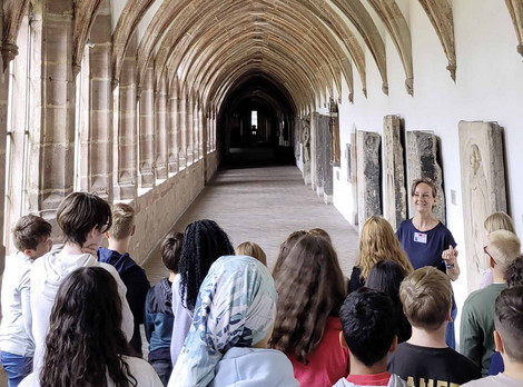 Klasse im Germanischen Nationalmuseum. Fotoaufnahme von Thomas Ruppenstein. Die Abbildung zeigt eine Schulklasse im Germanischen Nationalmuseum. Sie stehen im Kreuzgang, während eine Museumspädagogin ihnen diesen erläutert. Die Fotoaufnahme stammt von Thomas Ruppenstein.