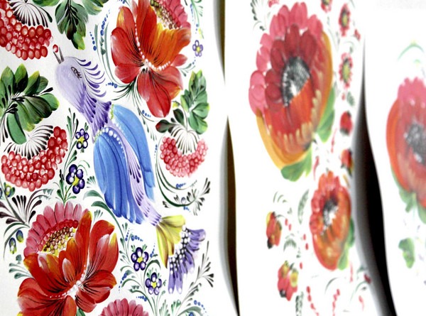 Die Abbildung zeigt verschiedene im Stil der Petrykiwka-Malerei gestaltete Werke. Zu sehen sind farbintensive Blumen und Vögel. Die Fotoaufnahme stammt von Kateryna Chebotarova.
