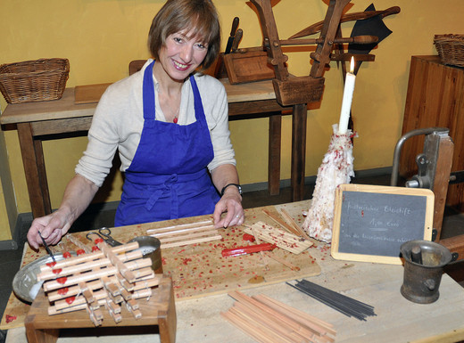 Die Abbildung zeigt eine Frau bei der Herstellung von Bleistiften, wie sie in früheren Zeiten von Hand gefertigt wurden. Die Fotoaufnahme stammt vom Museum Industriekultur.