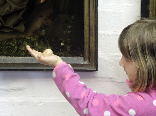 Die Abbildung zeigt ein Mädchen vor einem Gemälde, auf dem auch eine kleine Schnecke als verstecktes christliches Symbol der Wiederauferstehung abgebildet ist. Das Mädchen hält das Haus einer Weinbergschnecke in der Hand und hält es vergleichend neben die gemalte Schnecke. Die Fotoaufnahme stammt von Thomas Ruppenstein.