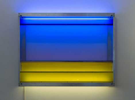 Die Abbildung zeigt das Kunstwerk Fair III, das der Künstler Reiner Bergmann im Jahr 1994 schuf. Es zeigt einen aus Kunststoff gefertigten Leuchtkasten, aus dem gelbes und blaues Licht scheint. Die Fotoaufnahme stammt von Annette Kradisch.