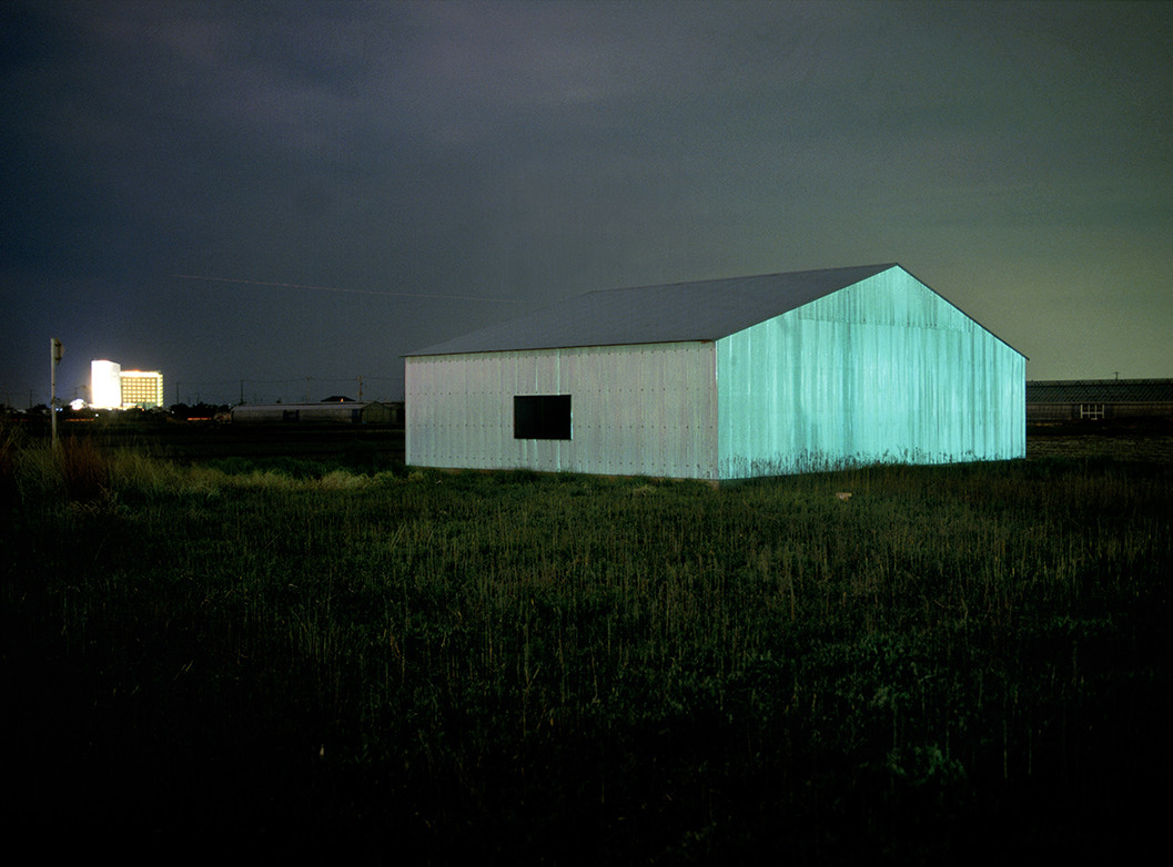 Die Abbildung zeigt eine Fotografie von Katsushito Nakazato aus der Serie  „De Chirico’s Shadow“. Es zeigt grün beleuchtetes Farmgebäude bei Nacht.